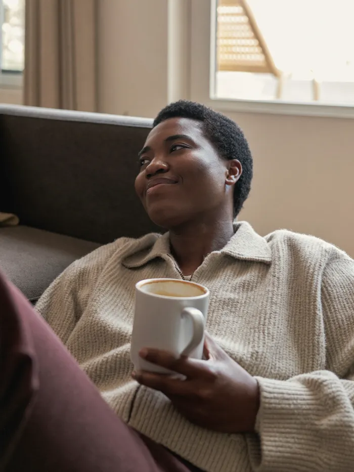 A person relaxing on their couch with a coffee, calm and content