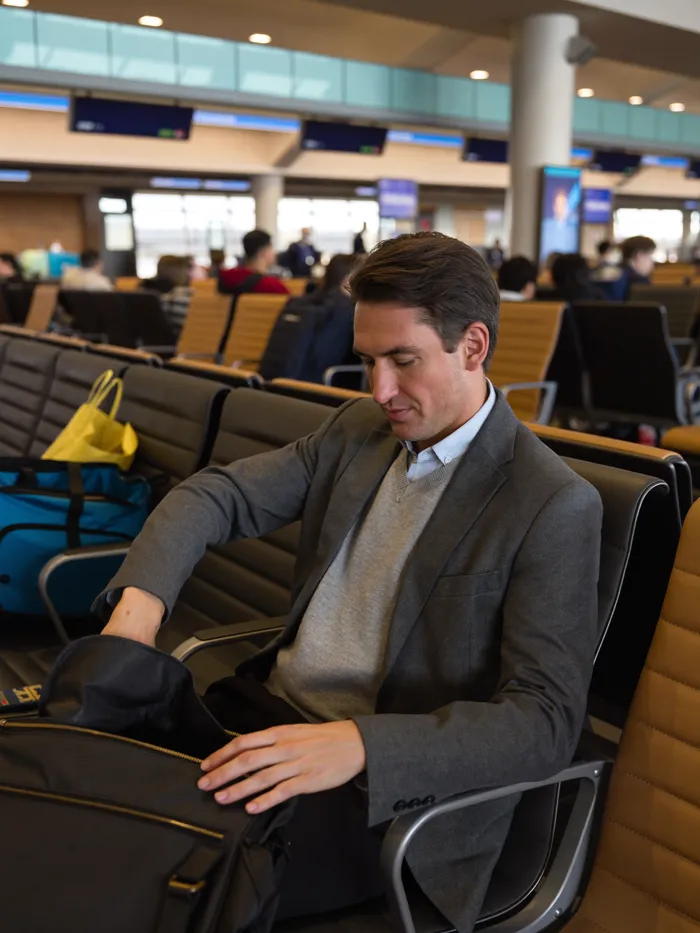 A man checking his phone in an airport terminal next to his travel bag